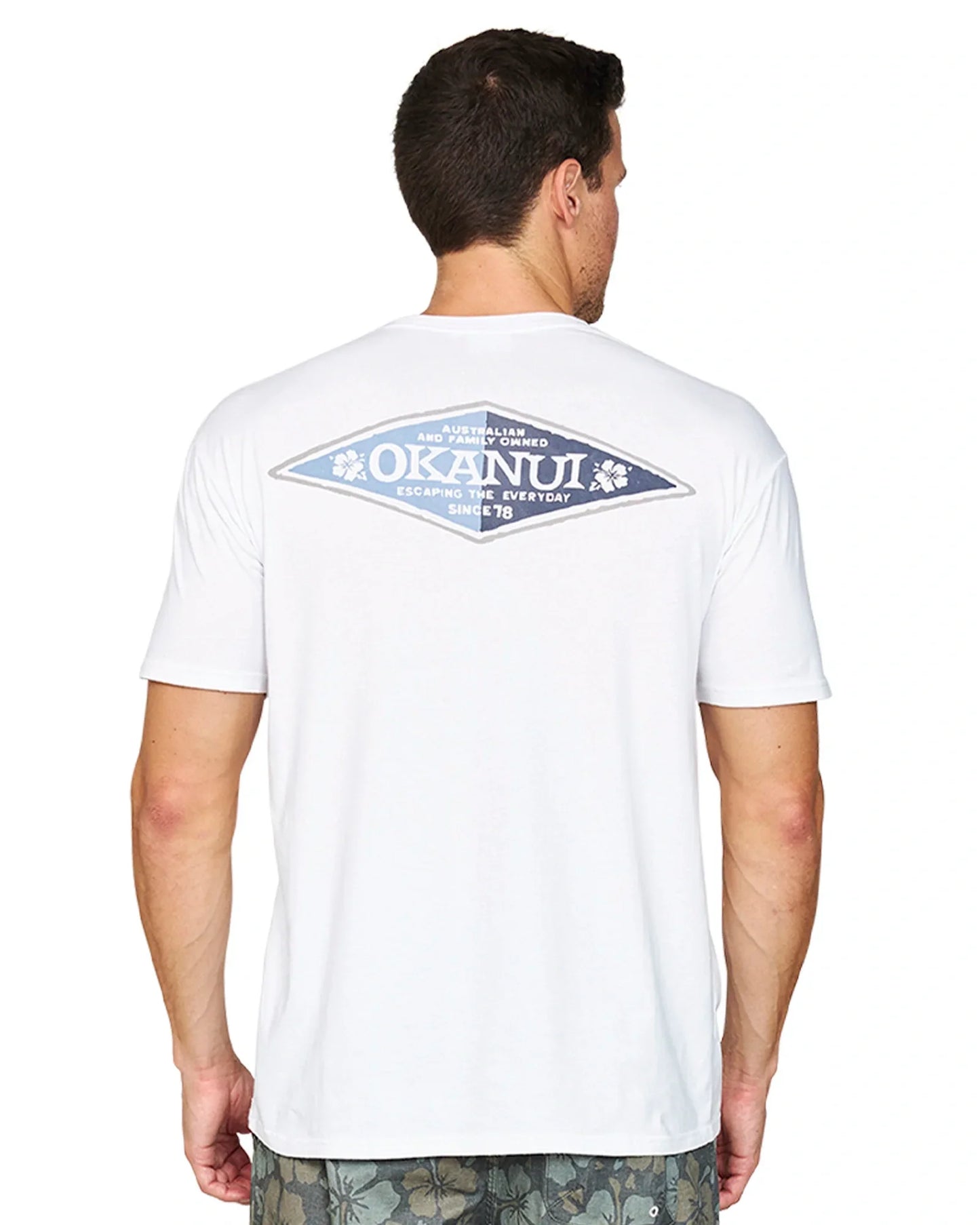 Closer back view of a male model wearing the Okanui Cornerstone T-shirt in white colour featuring a back print with "Okanui" on a rhombus multicolor shape.
