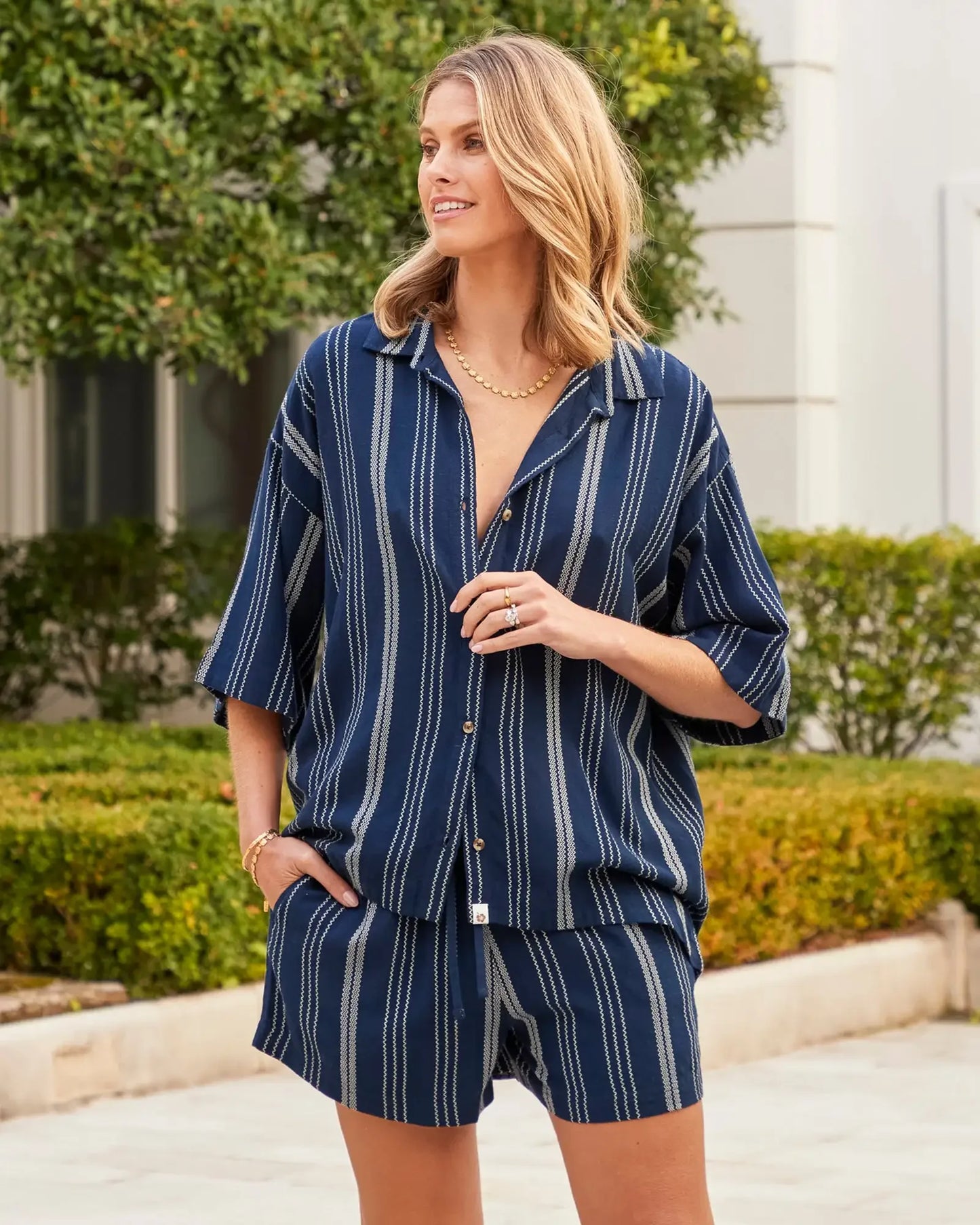 A female model posing wearing the Okanui women's Beach Short in navy stripe.
