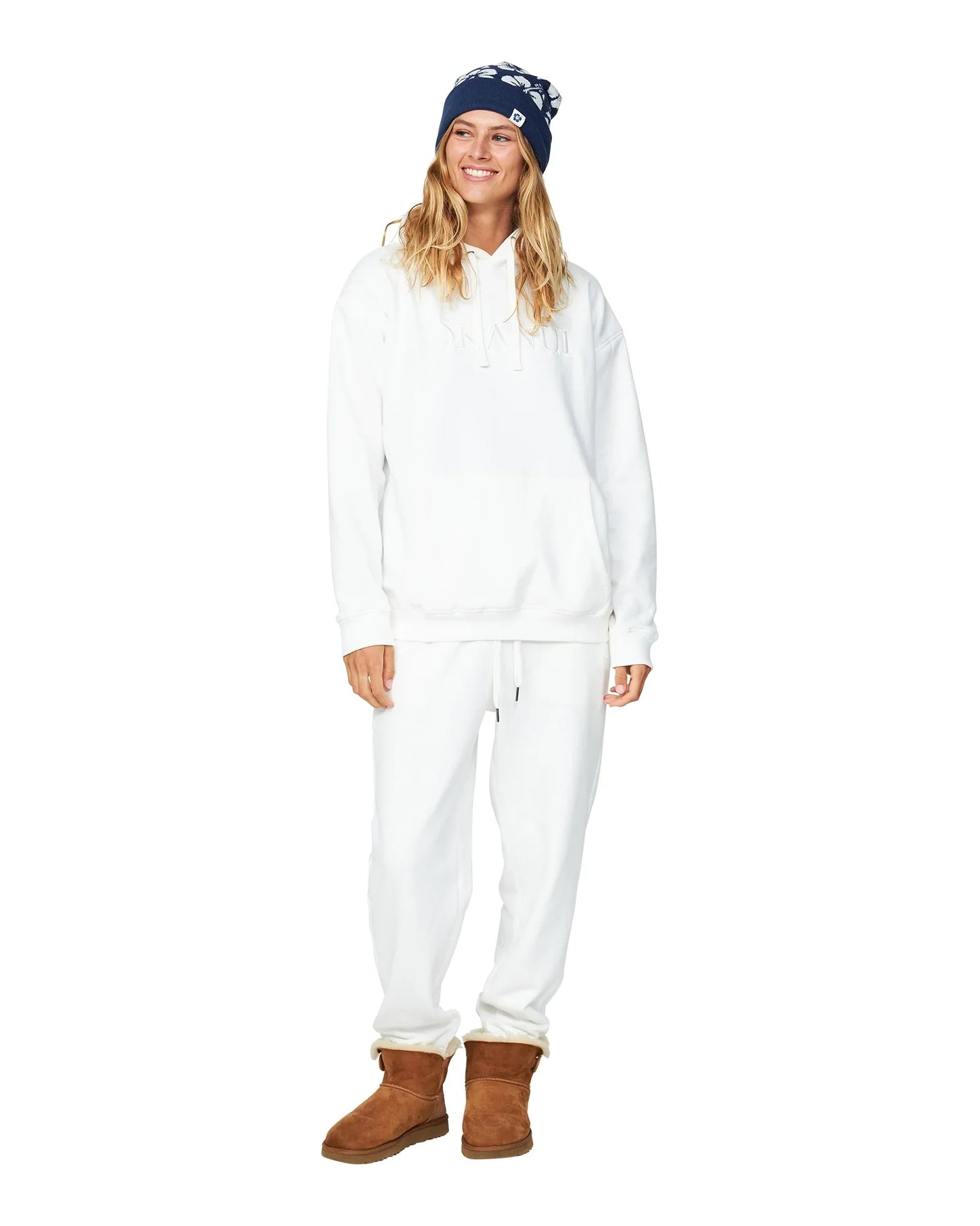 A woman is wearing an all white jacket and trackpants with navy blue hibiscus hat and brown boots.