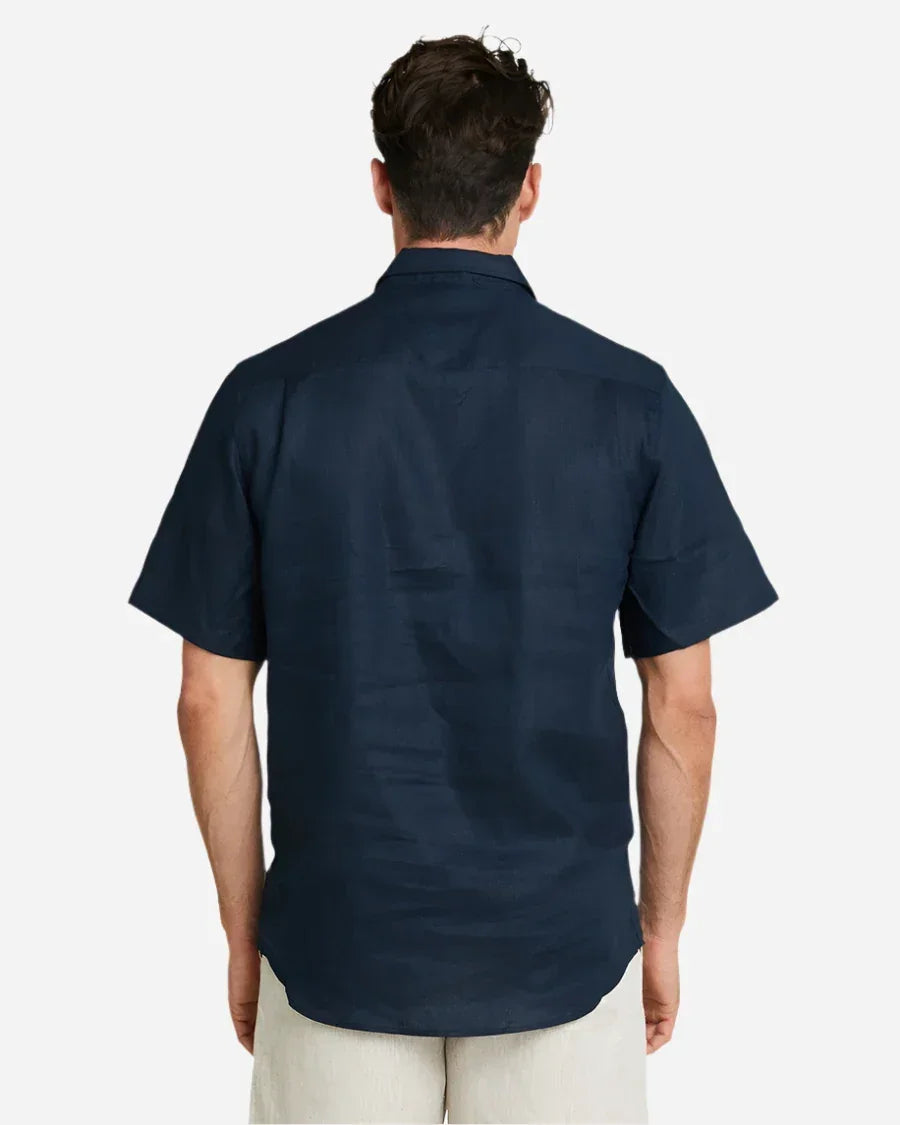 A back view of a male model posing and wearing the Okanui Linen Short Sleeve shirt in navy.