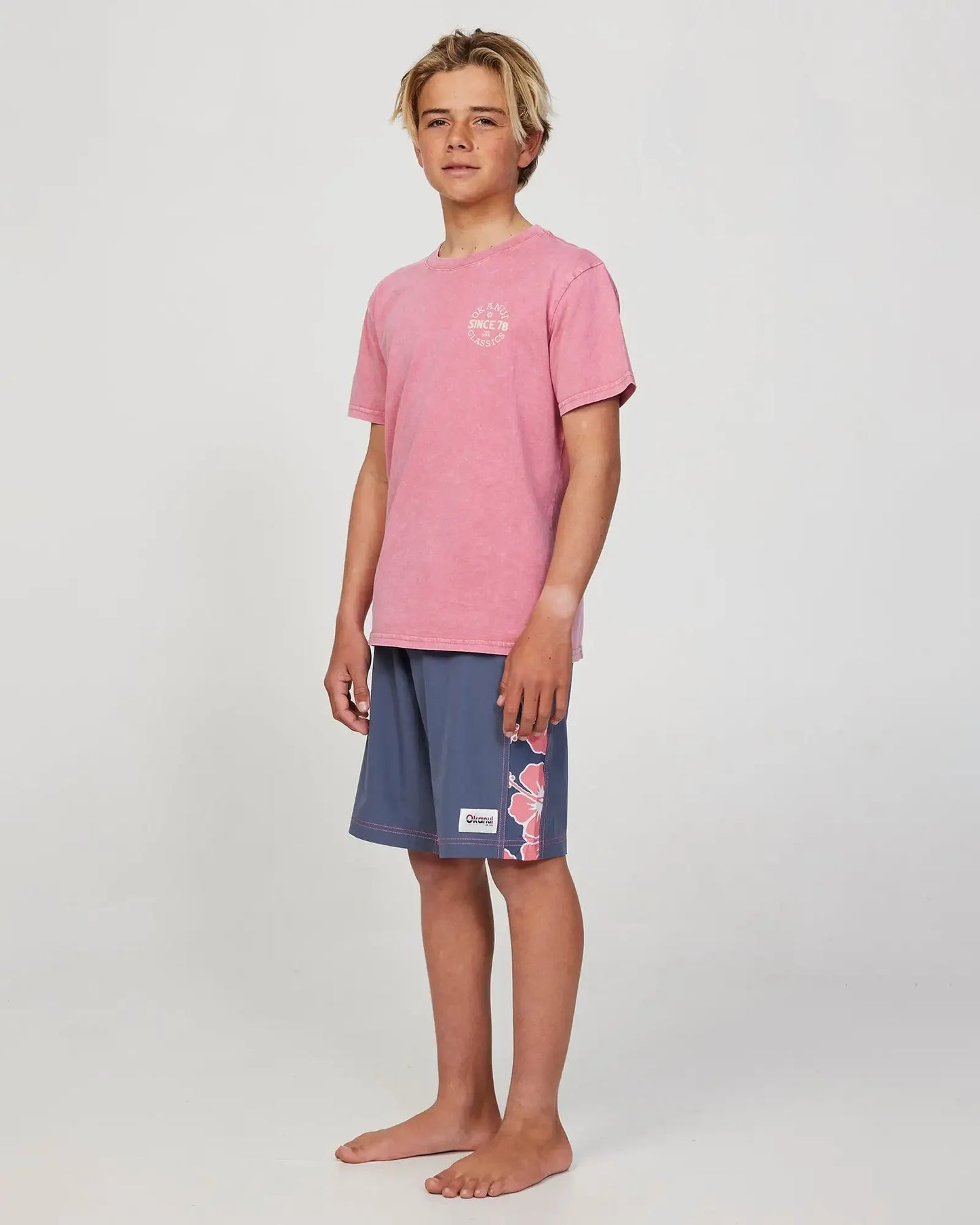Full body front view of a boy model wearing the Okanui Stamp Tshirt for boys in Washed Rose