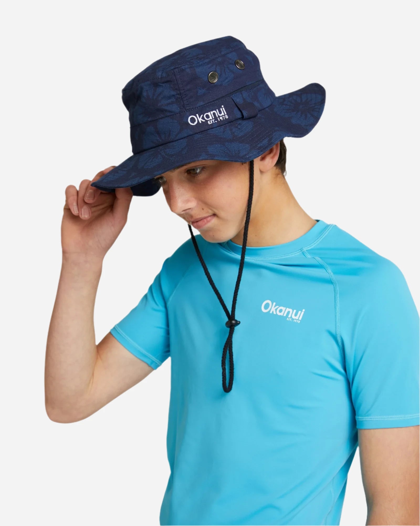 A young male model wearing a blue Okanui t-shirt and the Okanui Boonie Bucket Hat featuring its compatibility with kids.