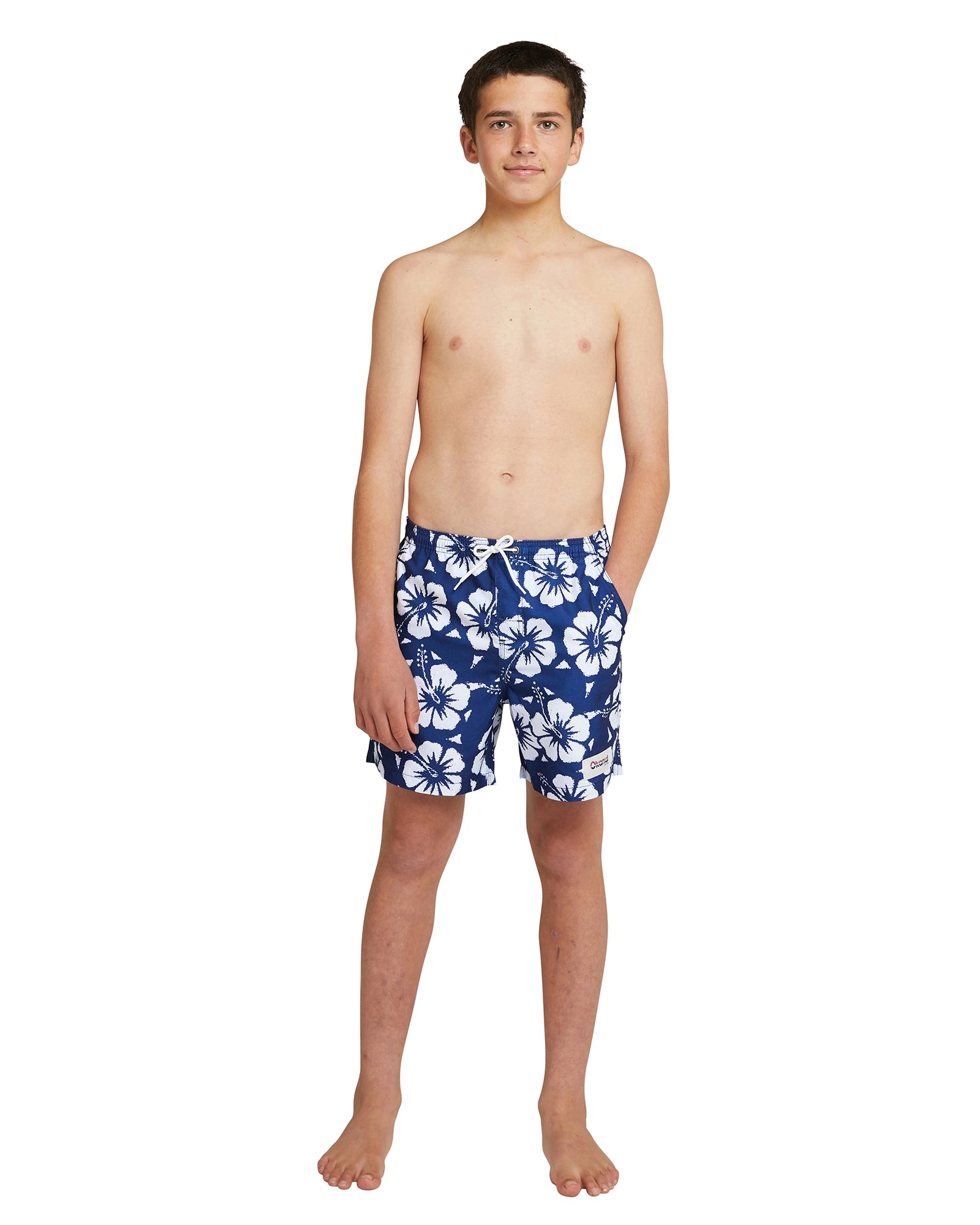 A topless boy wearing the Okanui boys swim shorts in Hibiscus Navy