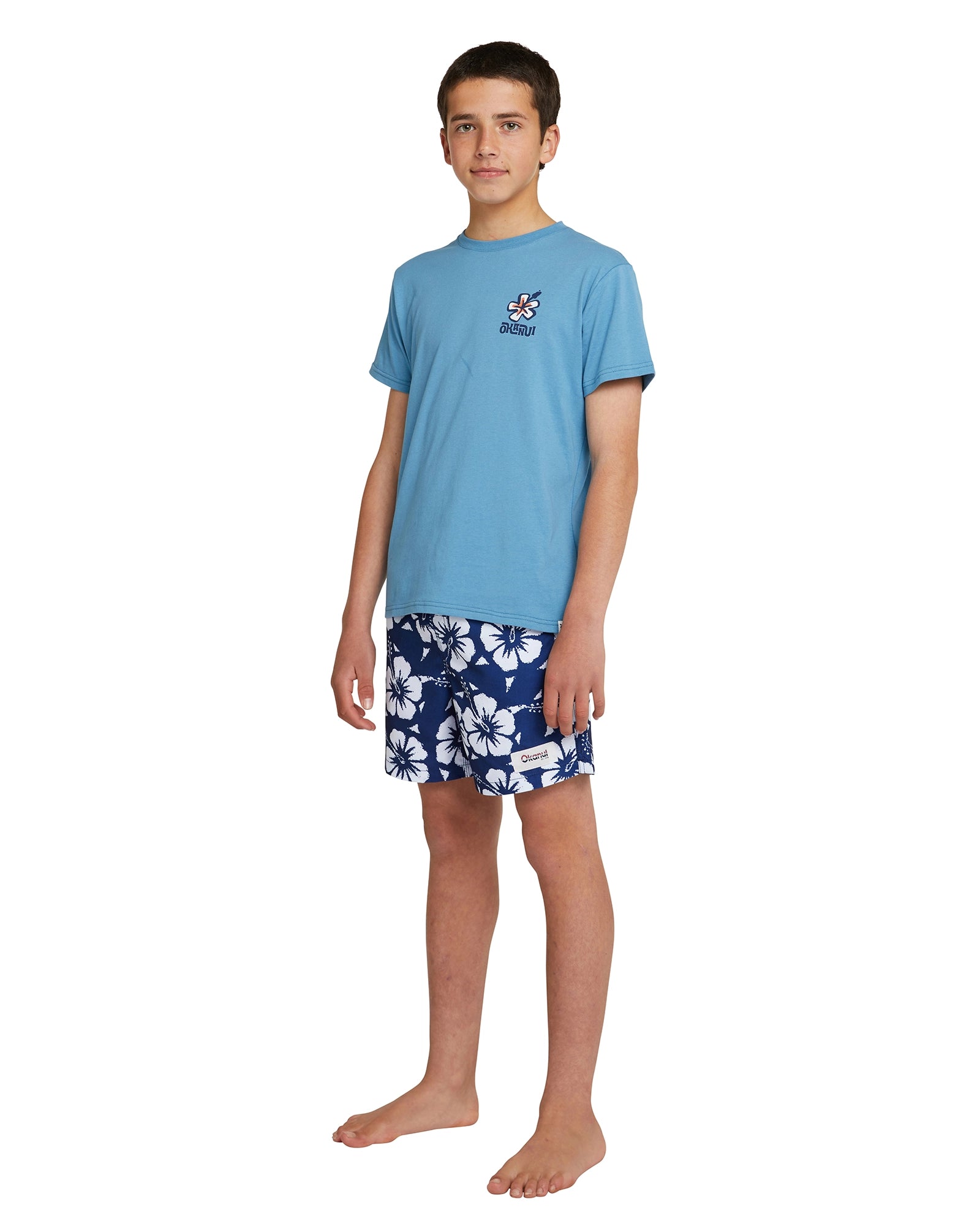 Angled front view of a boy wearing the Okanui boys swim shorts in Hibiscus Navy