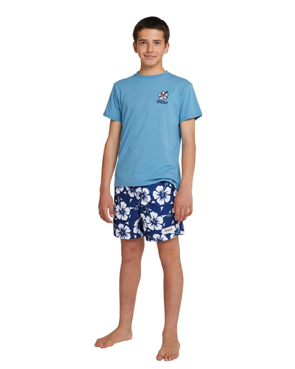 Full body front view of a boy wearing the Okanui boys swim shorts in Hibiscus Navy paired with T-shirt