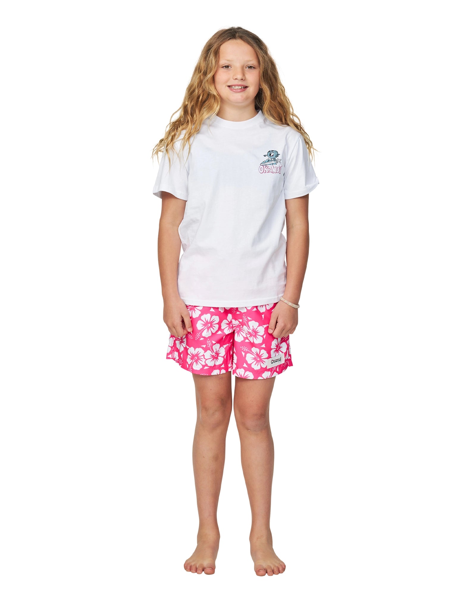 A girl in white T-shirt wearing the Okanui girls swim shorts in Hibiscus Hot Pink