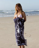 A female model in bikini covering her bottoms with the Okanui Classic Hibiscus Beach towel in Navy color