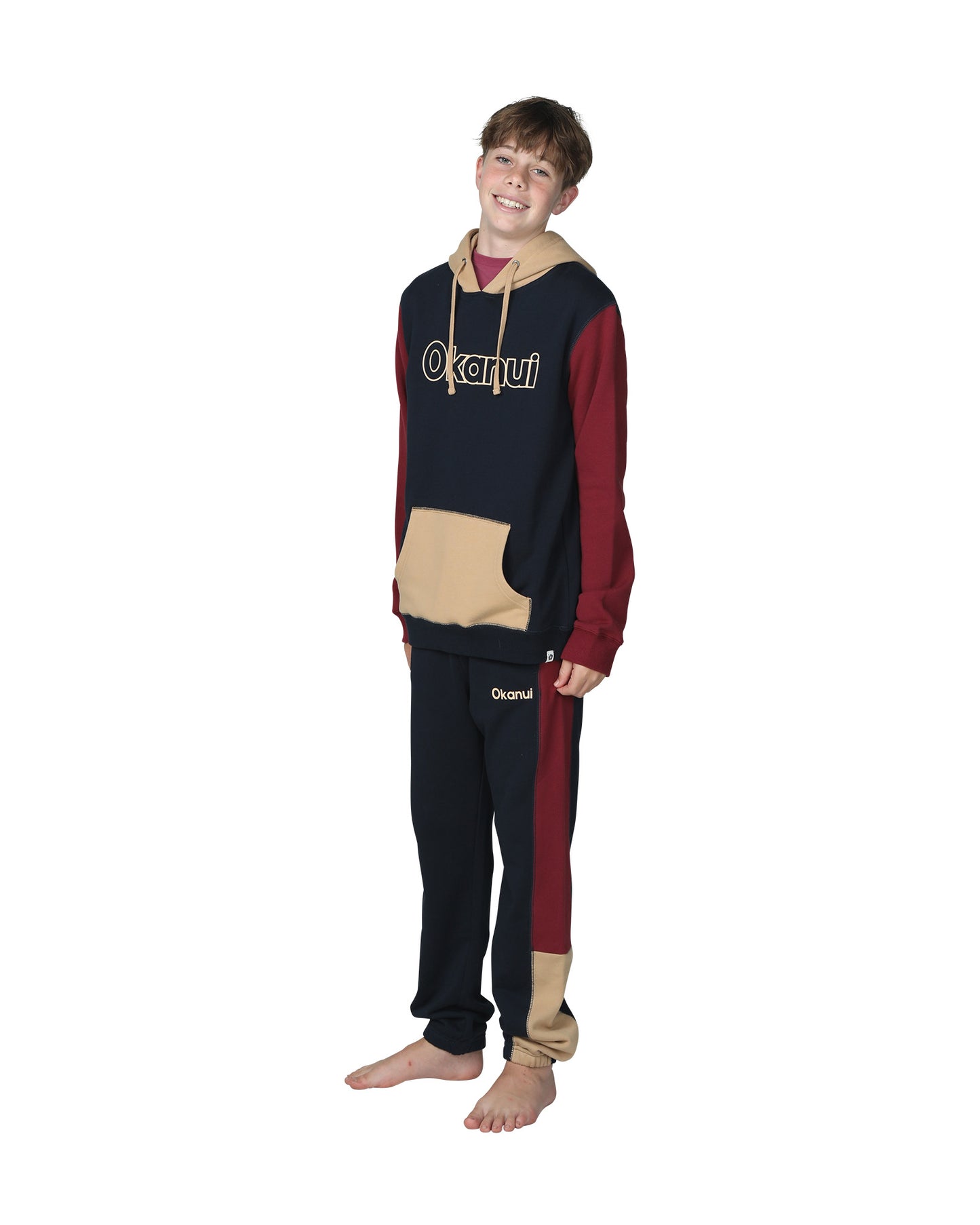 Full body front view of a boy wearing the Okanui Boys Track pants trackies in Navy Multi