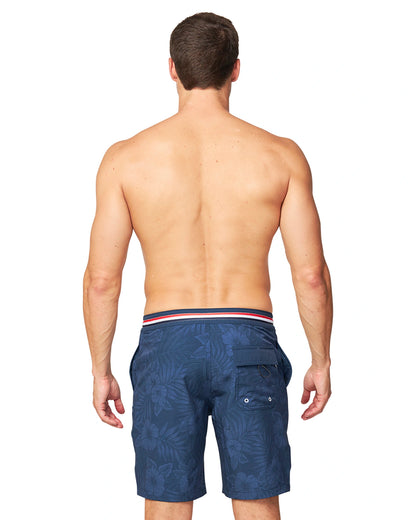 Back view of a model wearing the wearing the Okanui Midnight Jungle Boardrider Boardshort in navy color.