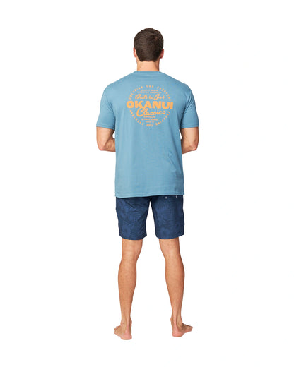 A back view of a male model wearing a blue t-shirt and the wearing the Okanui Midnight Jungle Boardrider Boardshort in navy color.