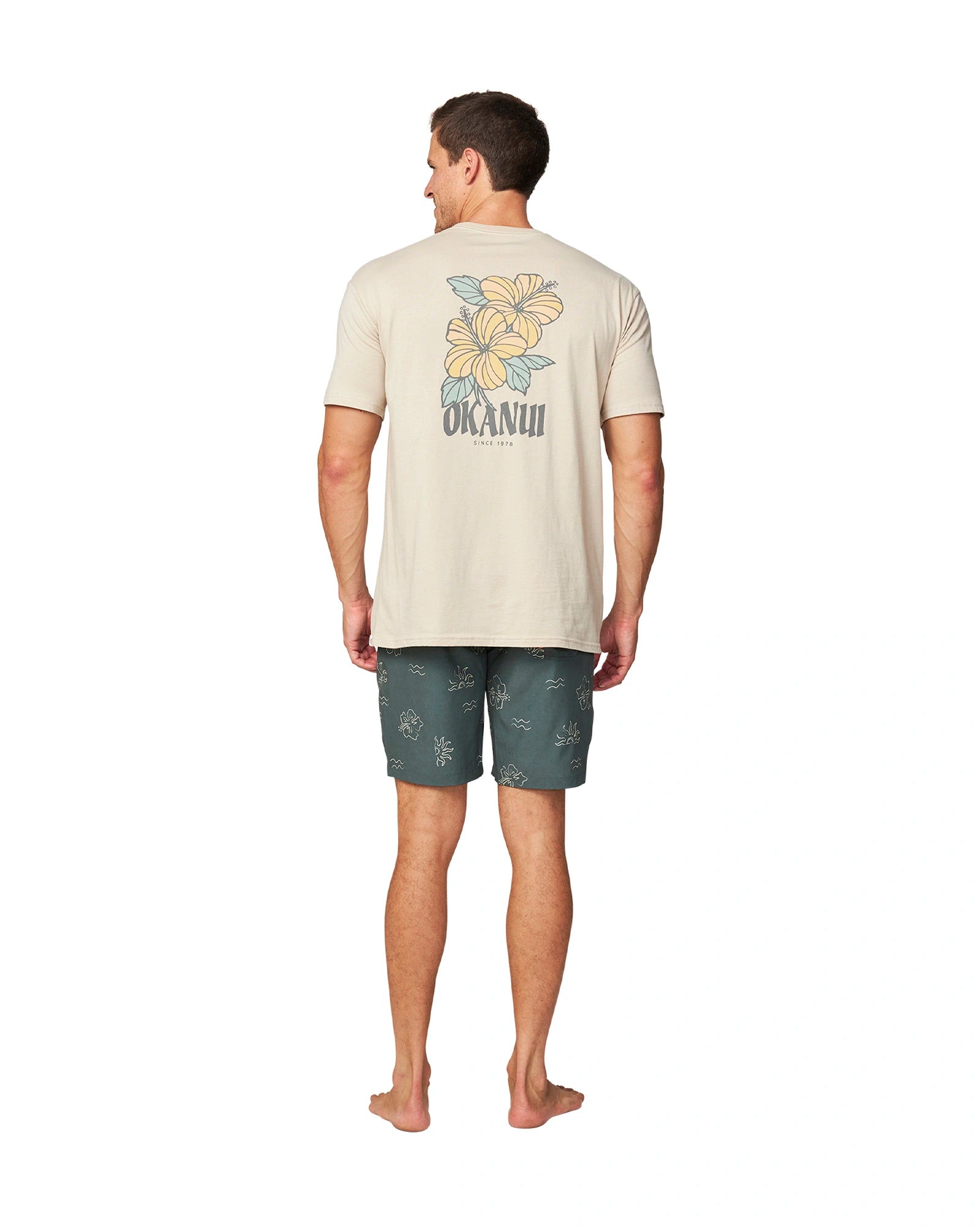 Back view of a male model wearing the Okanui Rising Sun Boardrider Boardshort in Forest color and a t-shirt showcasing the back print.