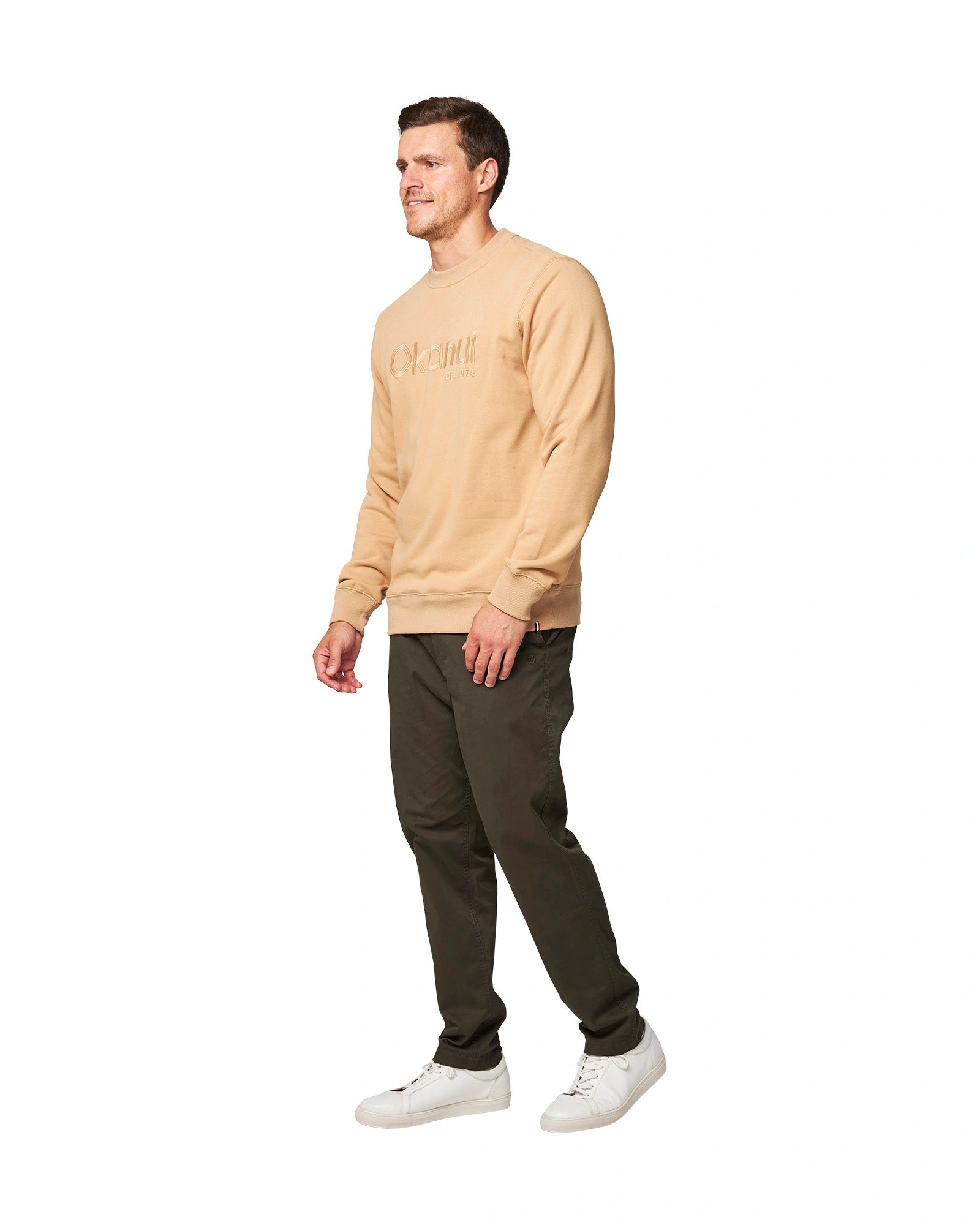 A man dressed in dark pants, white shoes, and a beige sweatshirt top facing the right side. 