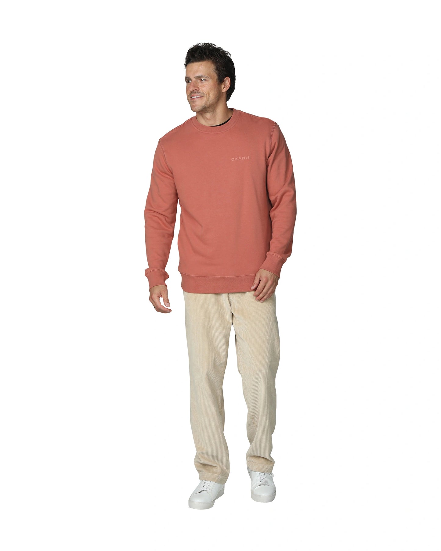 Wearing a rust-colored sweatshirt with light-colored pants and white shoes.