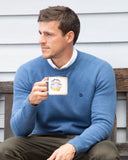 Okanui Anchor Knit in Blue Marle color worn by a model posing outside a house drinking coffee.