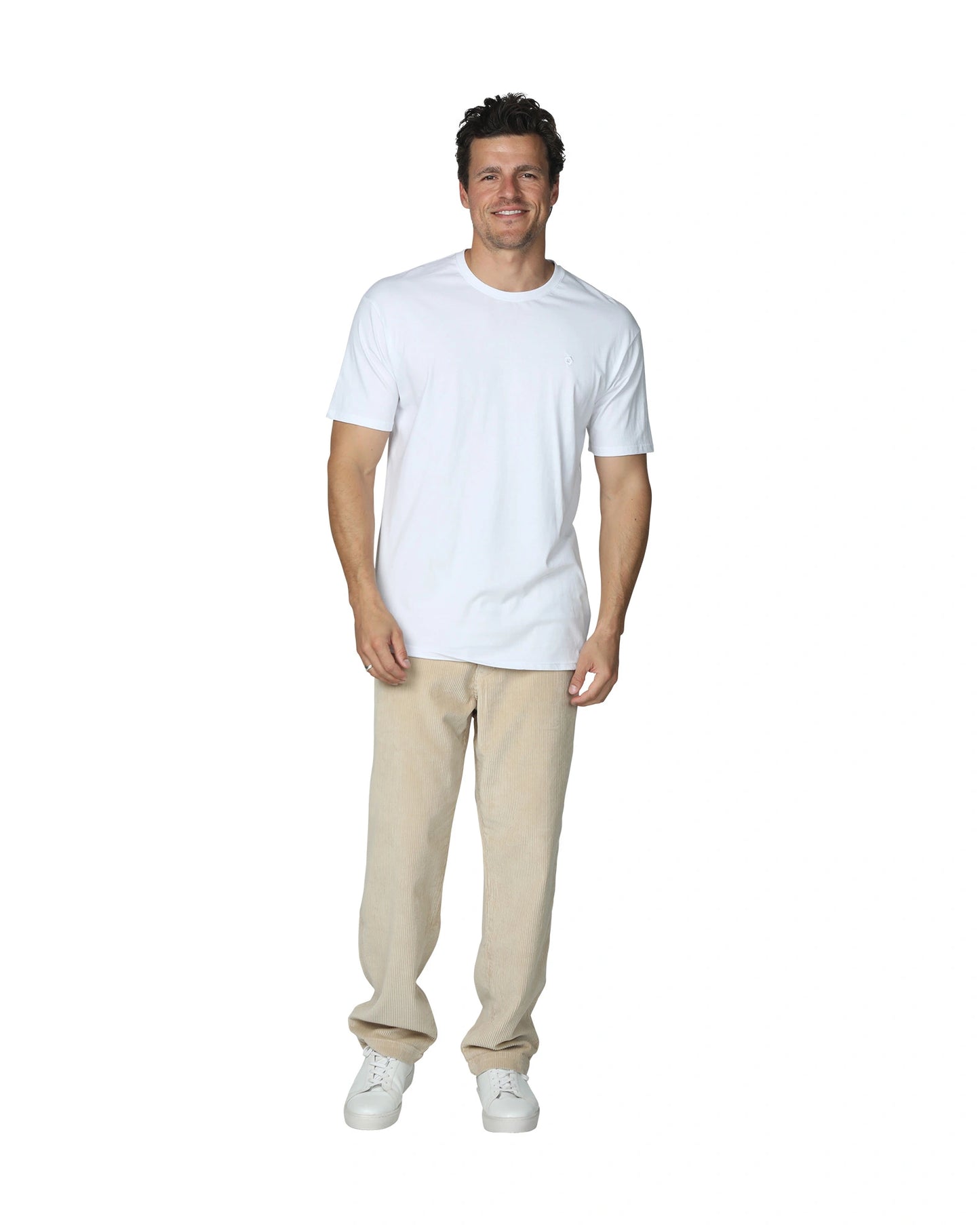 A male model wearing a plain white t-shirt and the Okanui Bay Corduroy Pant in Oat colour.