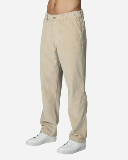 A slightly side view of a male model wearingthe Okanui's Bay Corduroy Pant in Oat colour.