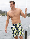 A male model holding a post, wearing the Okanui Way Back When stretch swim shorts in Navy Lime color
