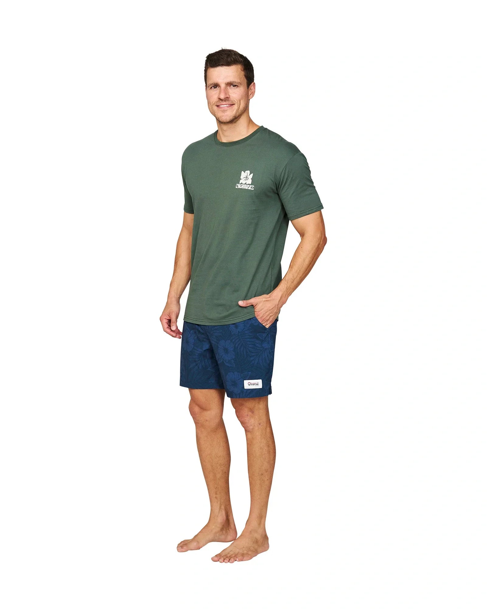 A male model wearing the Okanui Jungle T-Shirt in Forest Colour with his hand in one pocket.