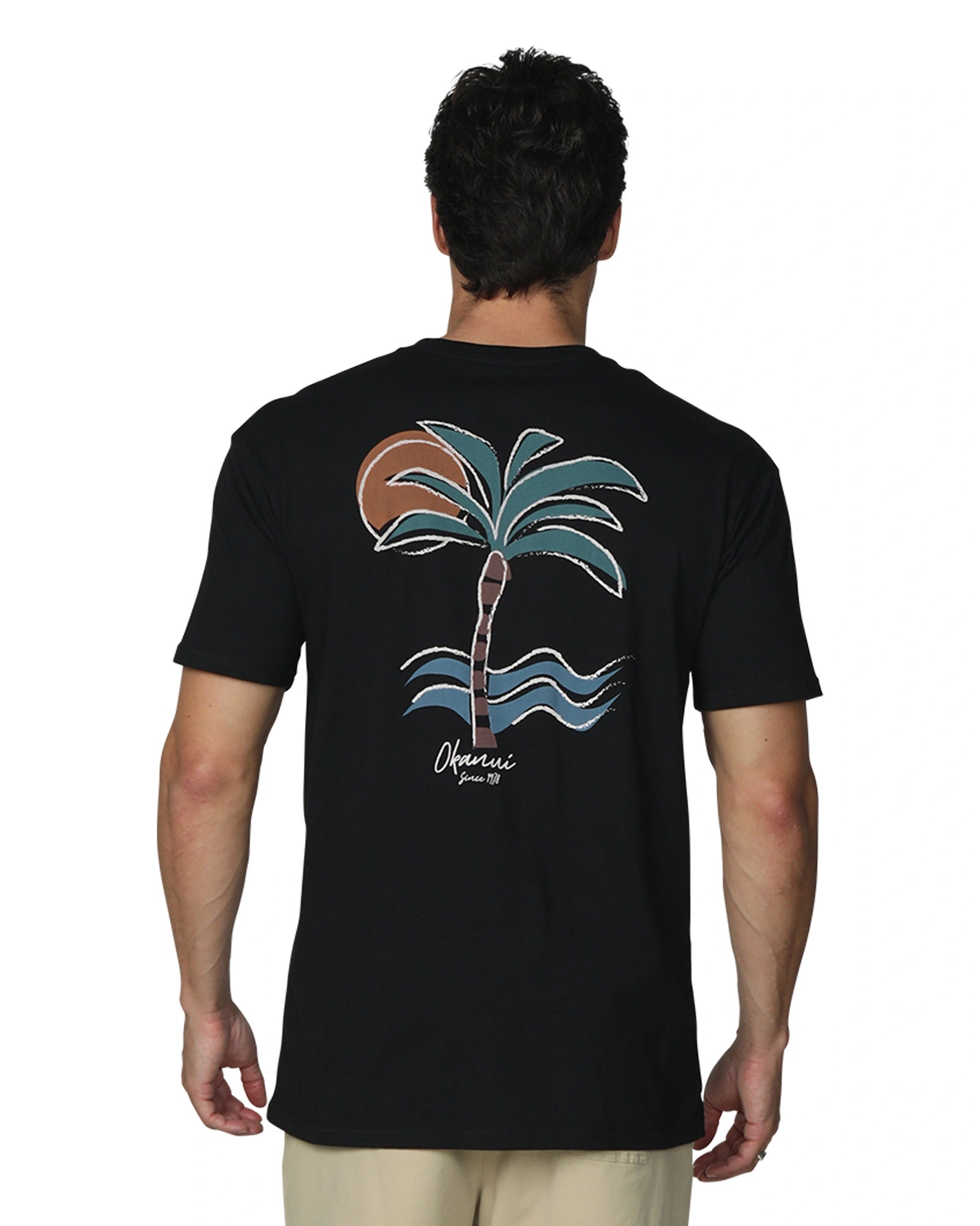 A close up back view of a male model front view wearing the Okanui's Island Nights T-Shirt in Black colour featuring the back print of a cartoonish palm tree, ocean waves, and the Sun.