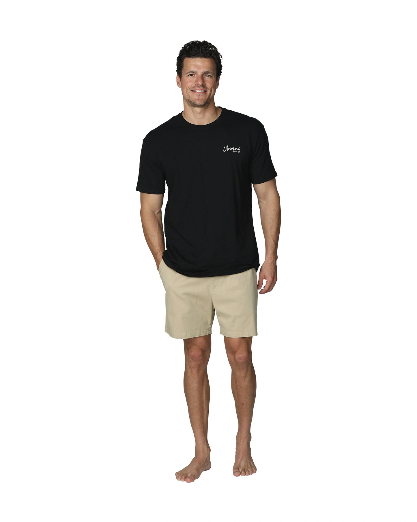 A full front view of a male model wearing the Okanui Island Nights T-Shirt in Black colour paired with a khaki walkshort.