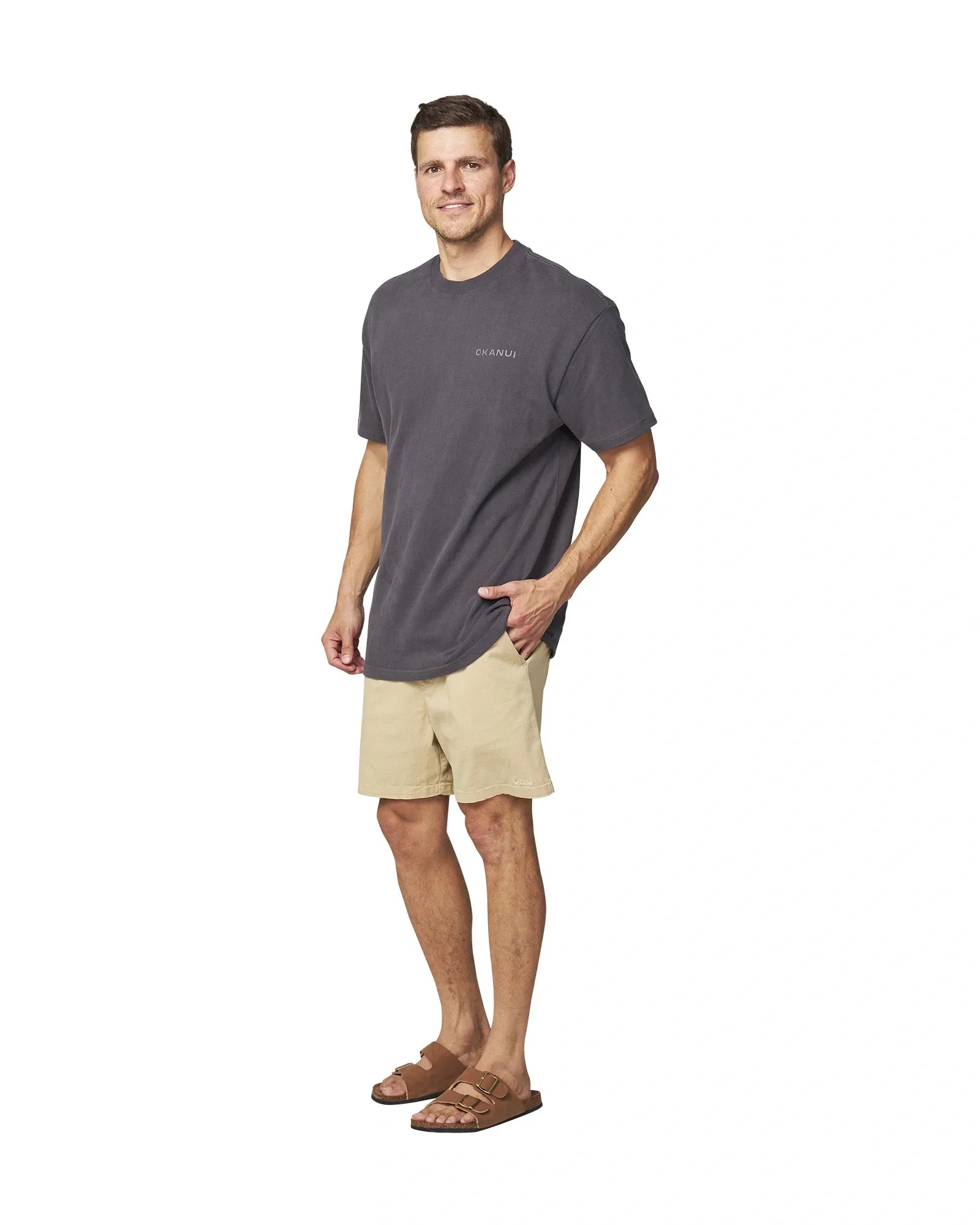Side full view of the Okanui Men's Cube Heavy Weight Tee in Washed Iron colour paired with walkshorts and slippers.