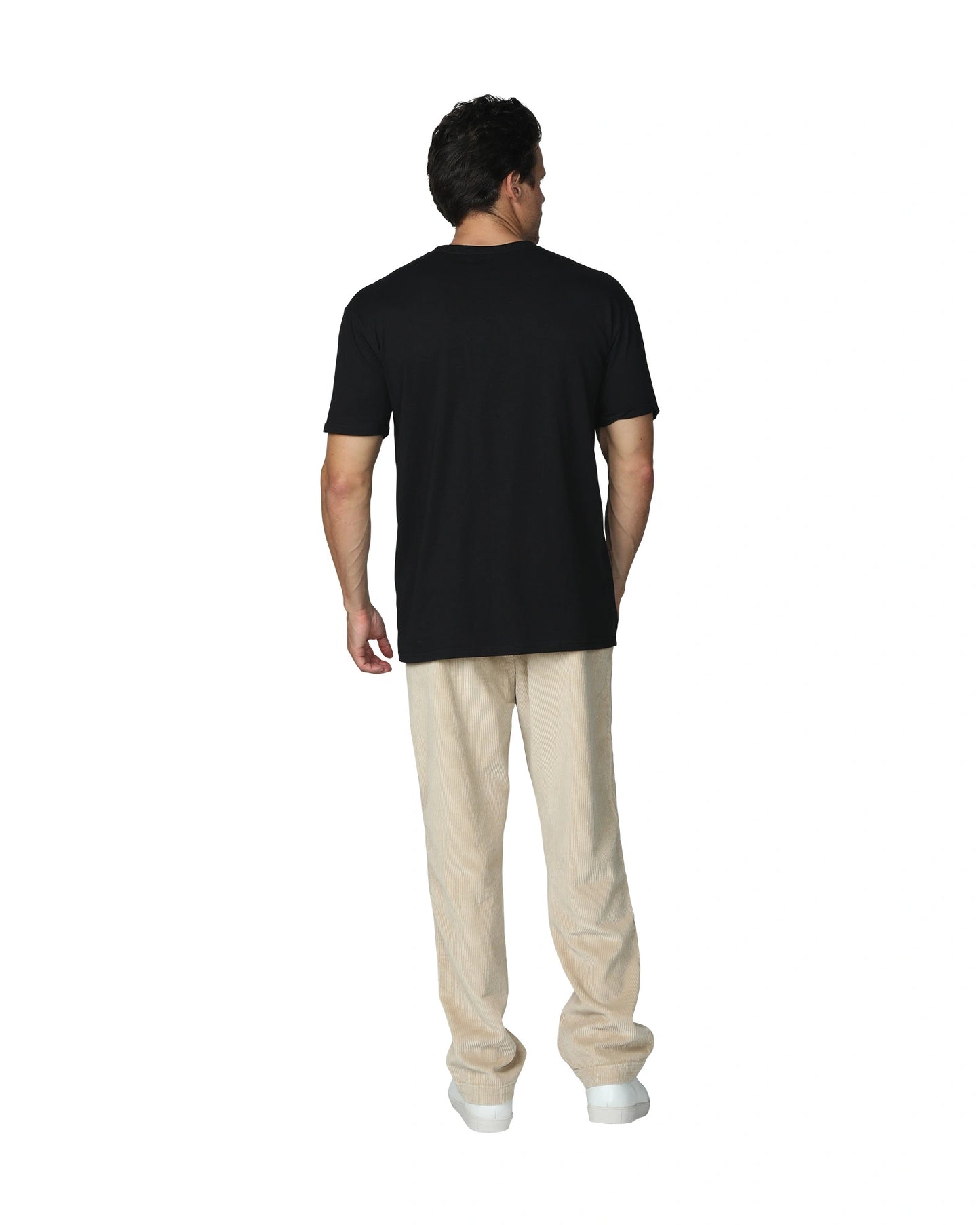 A full back view of a male model with his hand in his pocket wearing the the Okanui Mens Staple Tee in Black colour paired with a khaki corduroy pants and white shoes.