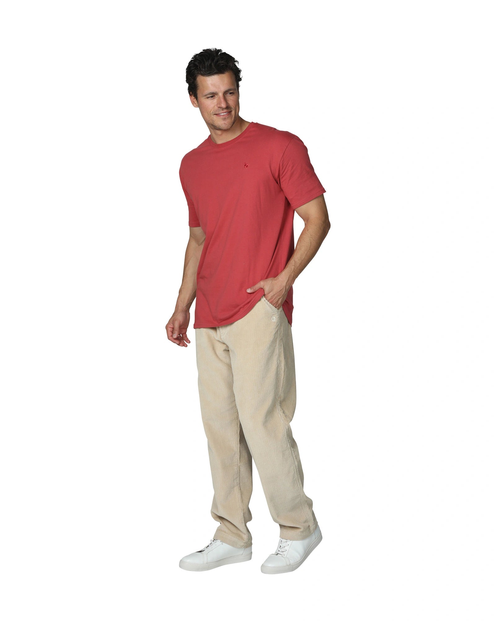 A full body view of a male model wearing the the Okanui Mens Staple Tee in Rust colour paired with khaki corduroy pants and white shoes.