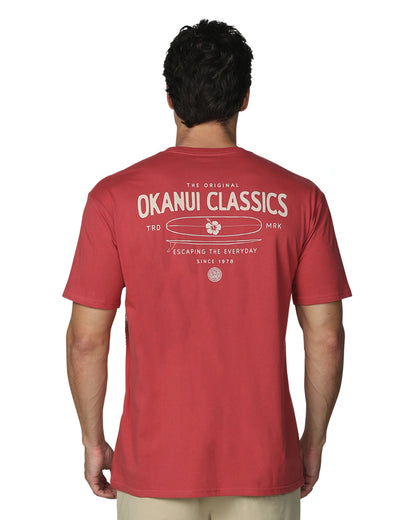 The close up back view of Okanui's Boardriders Men's T-Shirt in Rust colour featuring the back print with the words "Okanui Classics" in white font and a drawing of a surboard below it.