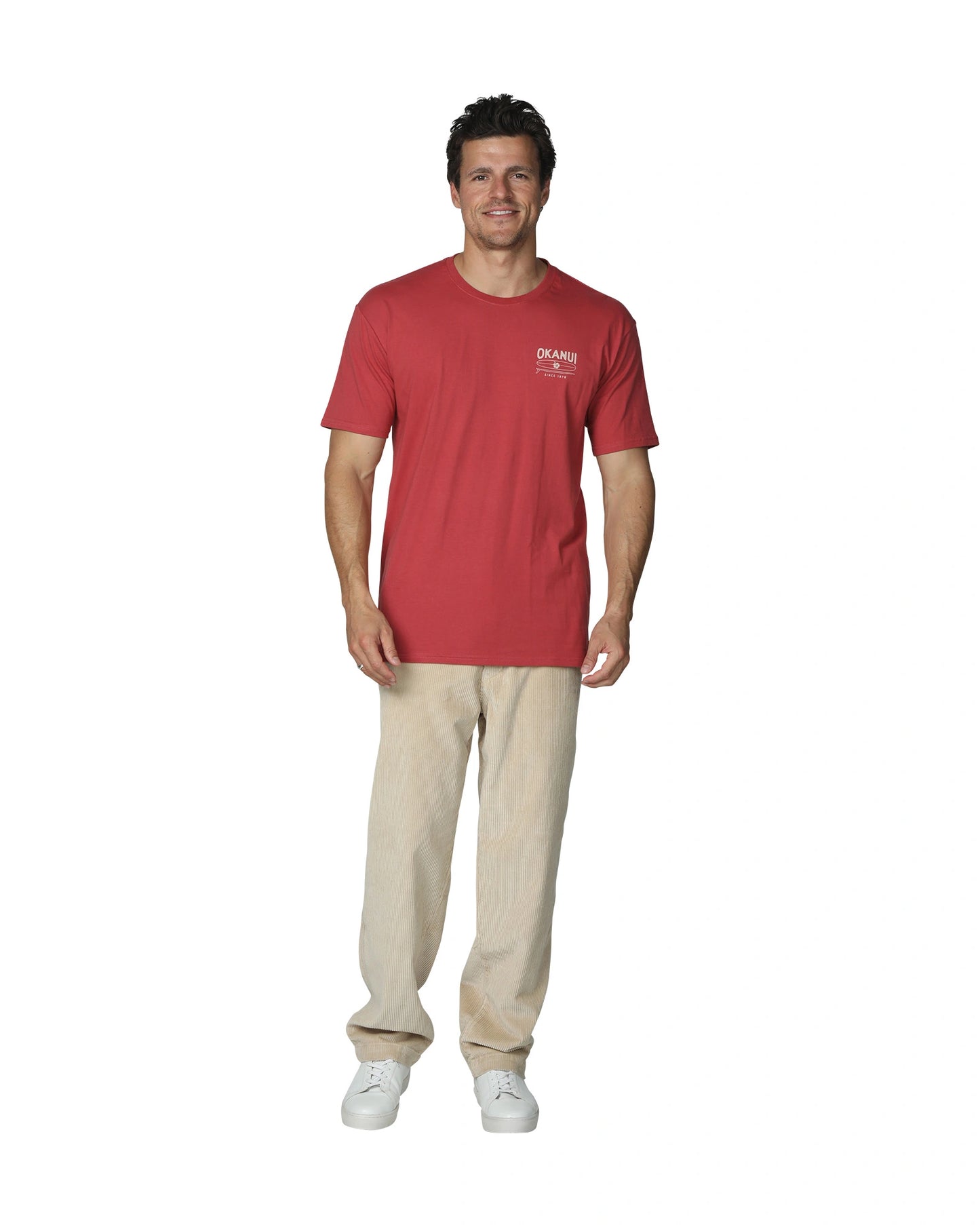 A full front view of a male model wearing Okanui's Boardriders Men's T-Shirt in Rust colour paired with a khaki corduroy pants and white shoes.