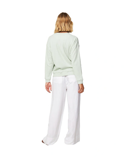 Full body back view of a female model wearing the Okanui long sleeve waffle knit jumper in gelato sage variant paired with a white trouser