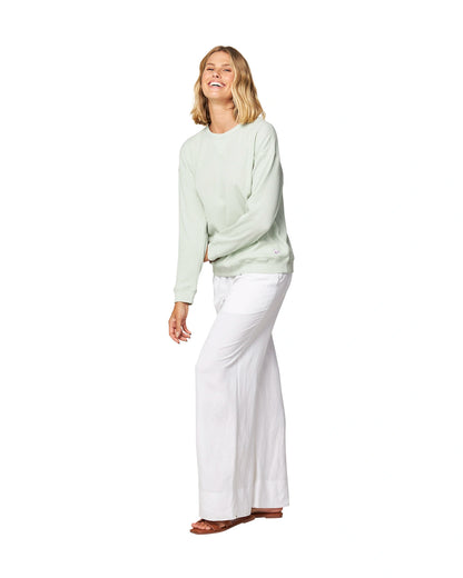 Cross arm pose of a female model wearing the Okanui long sleeve waffle knit jumper in gelato sage variant paired with a white trouser