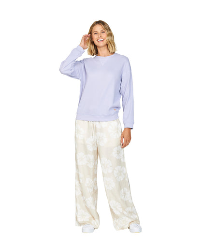 Full body of a female model with her hand in her hair, wearing the Okanui long sleeve waffle knit jumper in Gelato Lilac variant paired with the Okanui Hibiscus print trouser