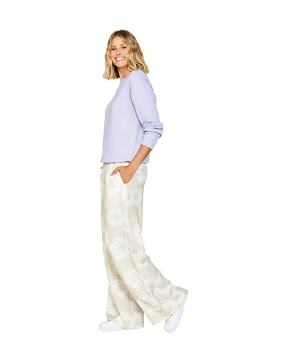 Left side view of a female model wearing the Okanui long sleeve waffle knit jumper in Gelato Lilac paired with a wide leg trouser in Okanui Hibiscus print