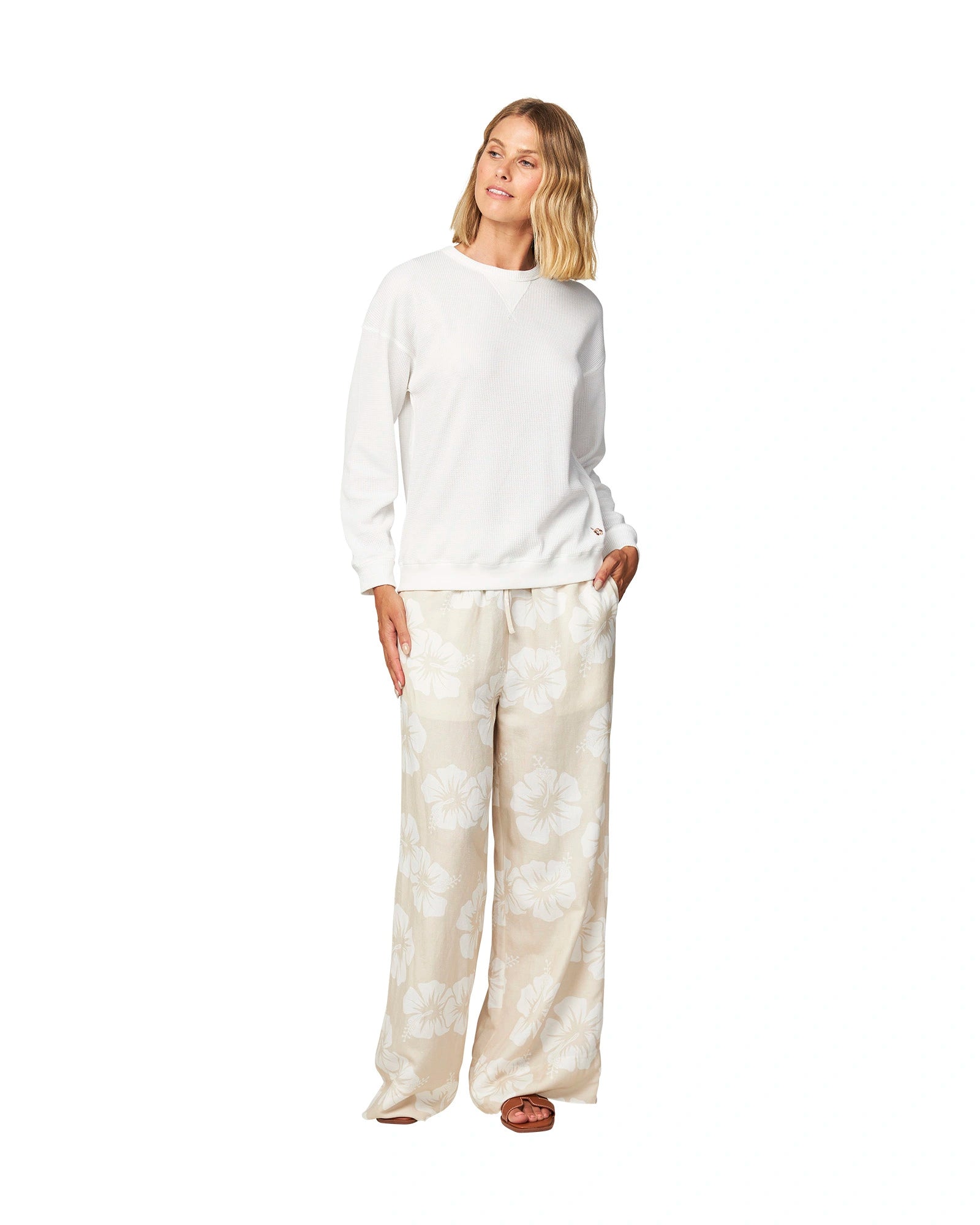 Full body front view of a female model wearing the Okanui long sleeve waffle knit jumper in white paired with an Okanui hibiscus trousers