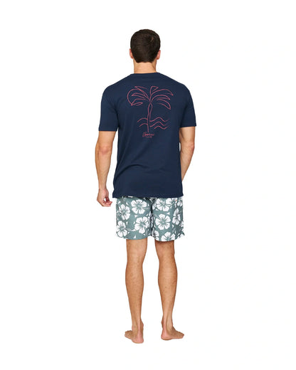 A full body back view of a model wearing a navy t-shirt with a print on the back and the Okanui Hibiscus Swimshorts in washed khaki color.