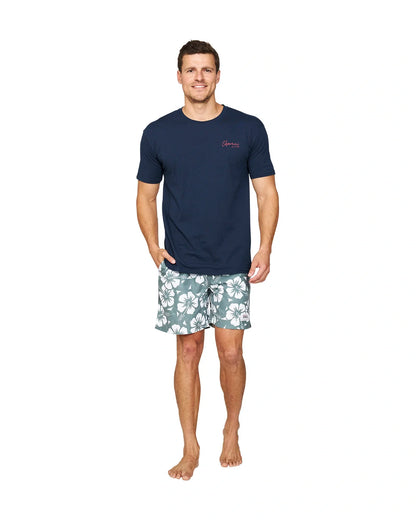 A full body view of a model wearing a navy t-shirt and the Okanui Hibiscus Swimshorts in washed khaki color.