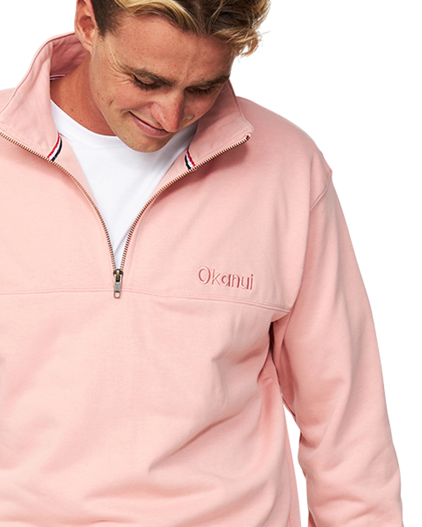 A closer view of a male model looking down pose wearing the Dusty Pink colour Okanui Clubhouse Crew Sweater putting emphasis on the chest logo.