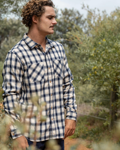 A male model posing candid outdoor wearing the Okanui Long Sleeve Flannel Hiker Shirt with bushes in the background.