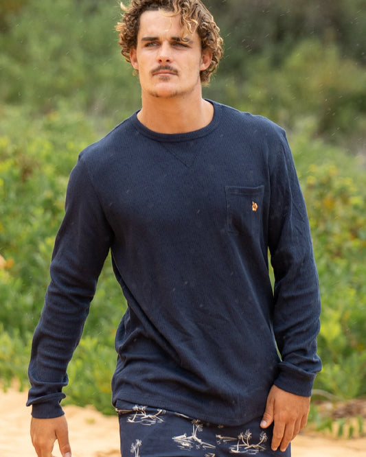 A male model with curly hair wearing the Okanui Long Sleeve Waffle Tee outdoors.