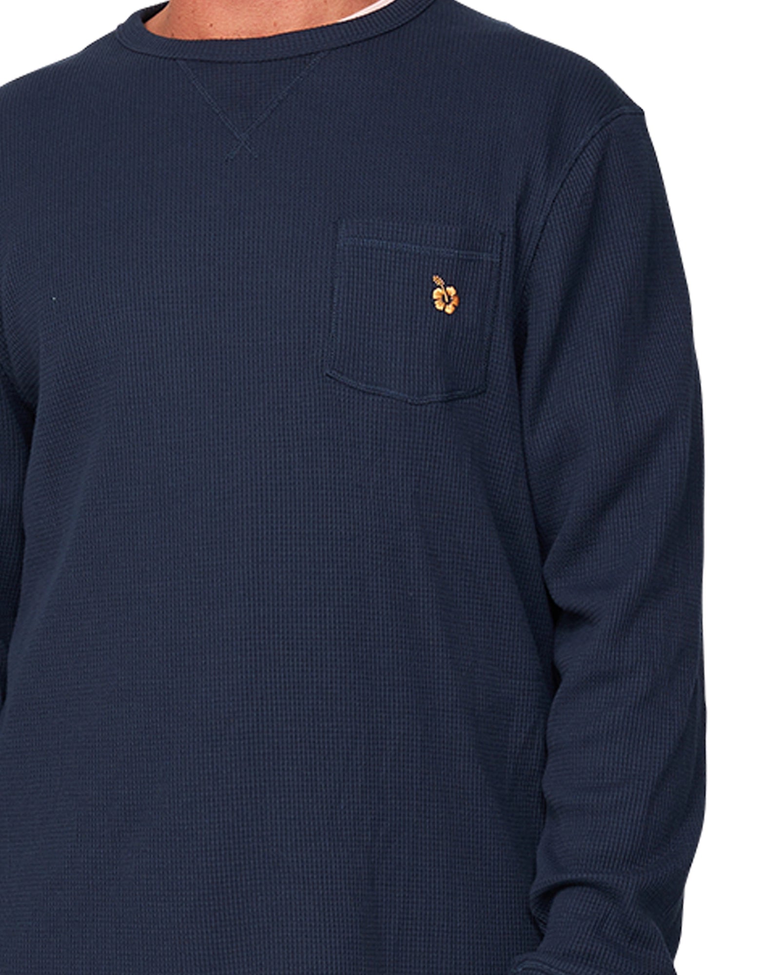 A close up view of the Okanui Long Sleeve Waffle Tee featuring the chest pocket and a small Hibiscus logo.