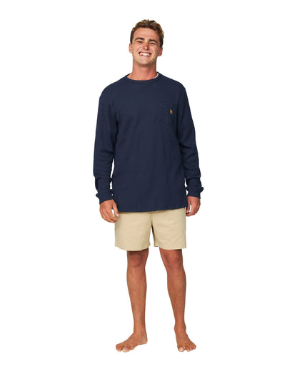 A whole body view of a male model wearing shorts and the Okanui Long Sleeve Waffle Tee in navy color.