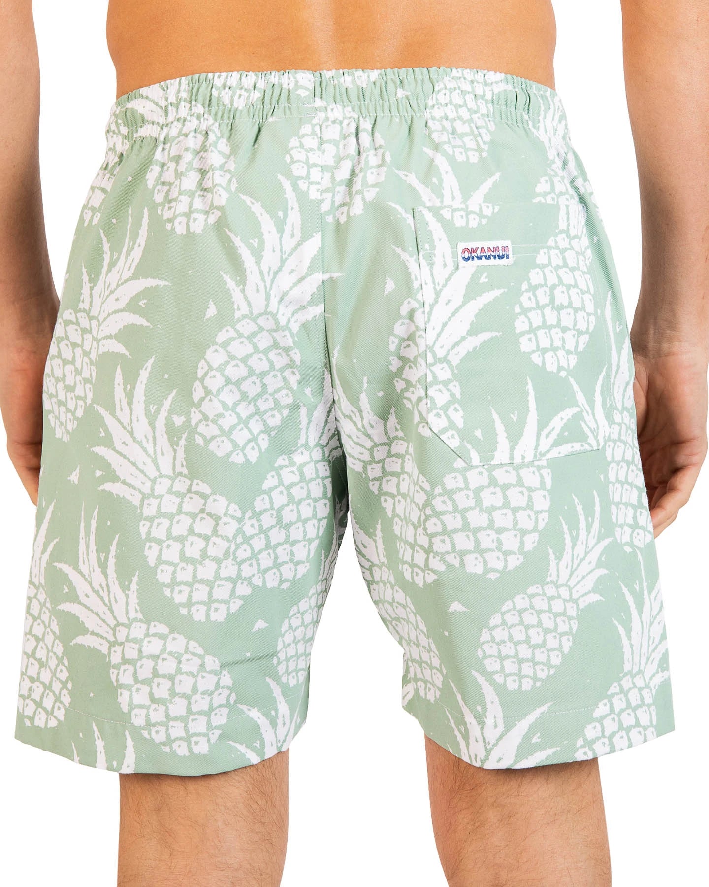 A classic men pair short shorts in white and mint green color showing the back part pocket with Okanui logo in color red and blue.