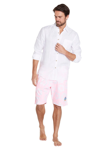 A man in a casual outfit is standing against a plain white background. He is wearing a white t-shirt and light pink shorts. He is barefoot and has a relaxed posture, looking slightly to his right.