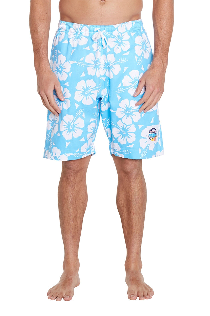 A person standing and wearing blue floral swim trunks with white flowers. The swim trunks have a drawstring at the waist and a small patch on the left leg. 