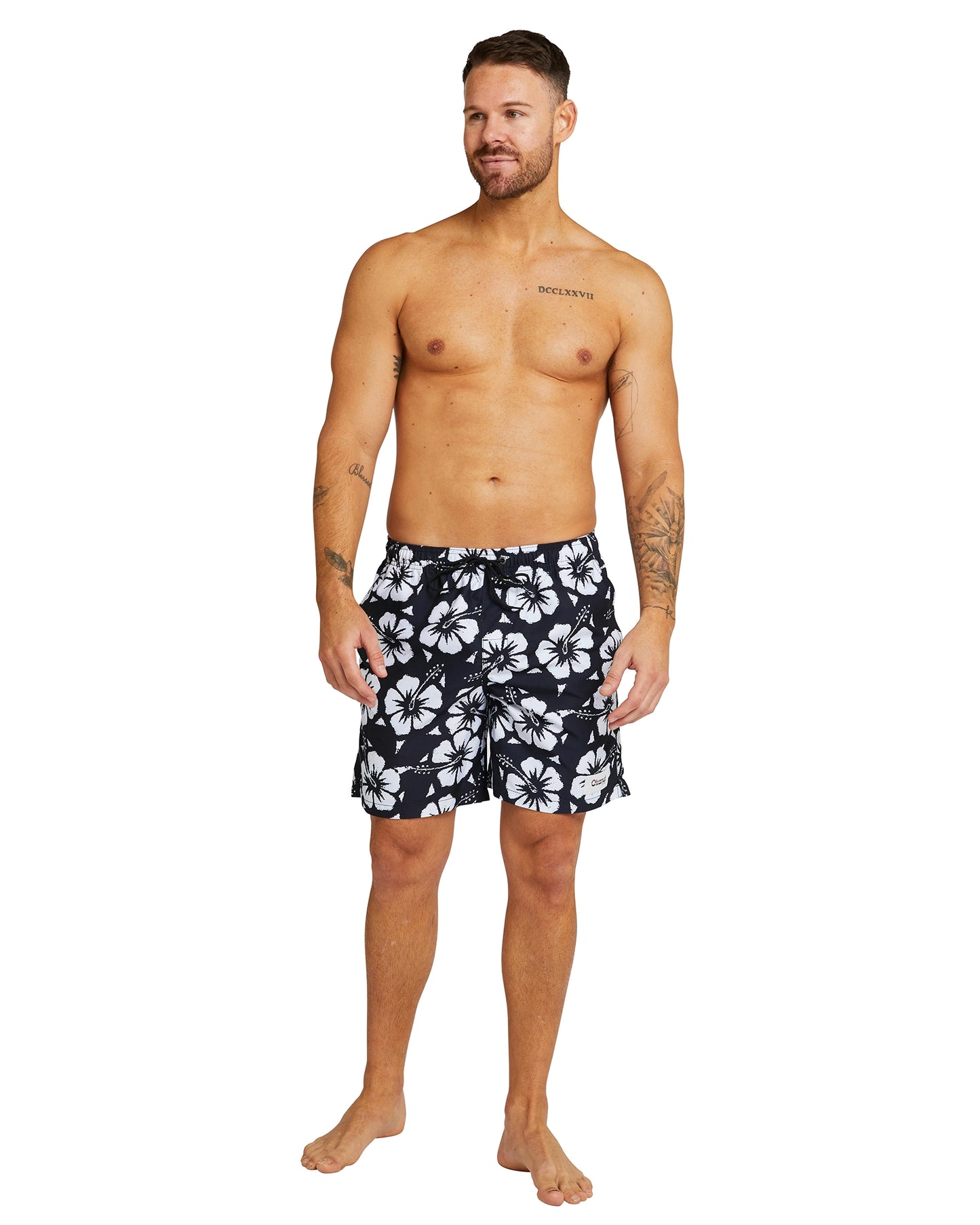 A shirtless male model wearing the Okanui Swimshorts in Hibiscus black.