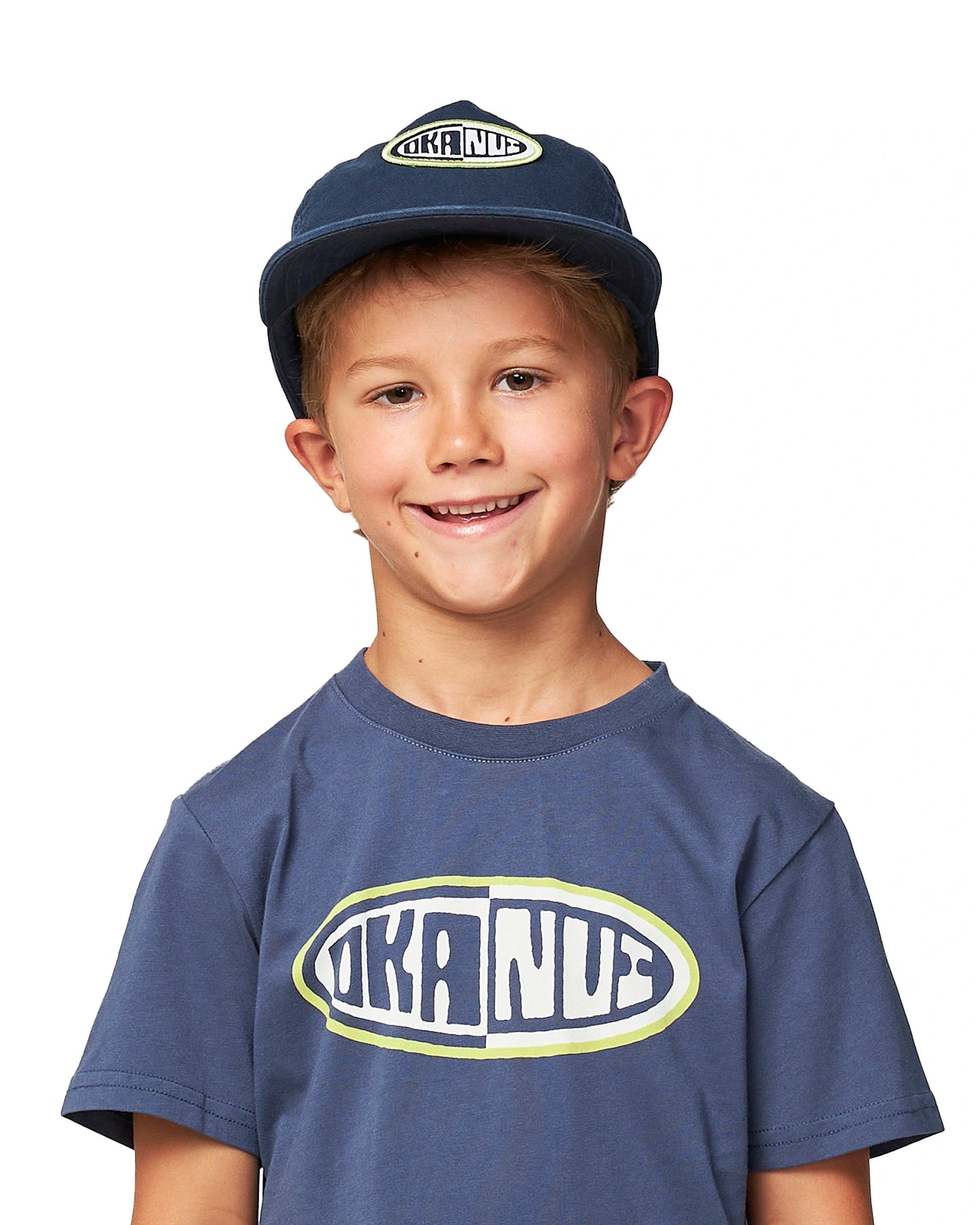 Front view of a young boy wearing the Washed Navy Okanui Deck Kids snapback trucker cap