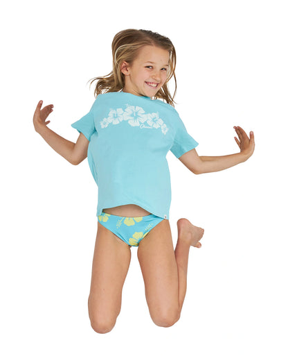 A girl jumping wearing the Okanui Logo Tee T-shirt in Washed Aqua