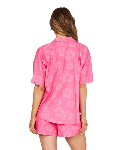 A closer back view of a female model wearing the Okanui Womens Classic Beach Short in Hibiscus Hot Pink paired with a terno loose fit shirt.