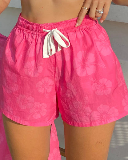 A close up lower view of a female model wearing the Okanui Classic Beach Short in Hibiscus Hot Pink.