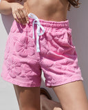 A close up lower view of a female model posing outside wearing the  Okanui Weekender Terry Short in Hibiscus Pink. 